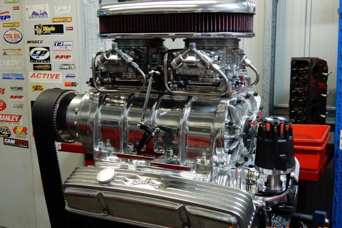 A Chrome Engine is Sitting on a Stand in Front of a Wall With Stickers on It — Aitkenvale Auto & Dyno in Aitkenvale, QLD