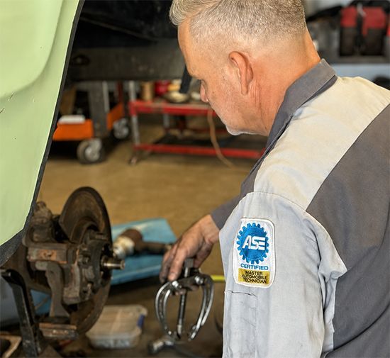 Mechanic working on a car brake in a garage, wearing a gray work shirt.