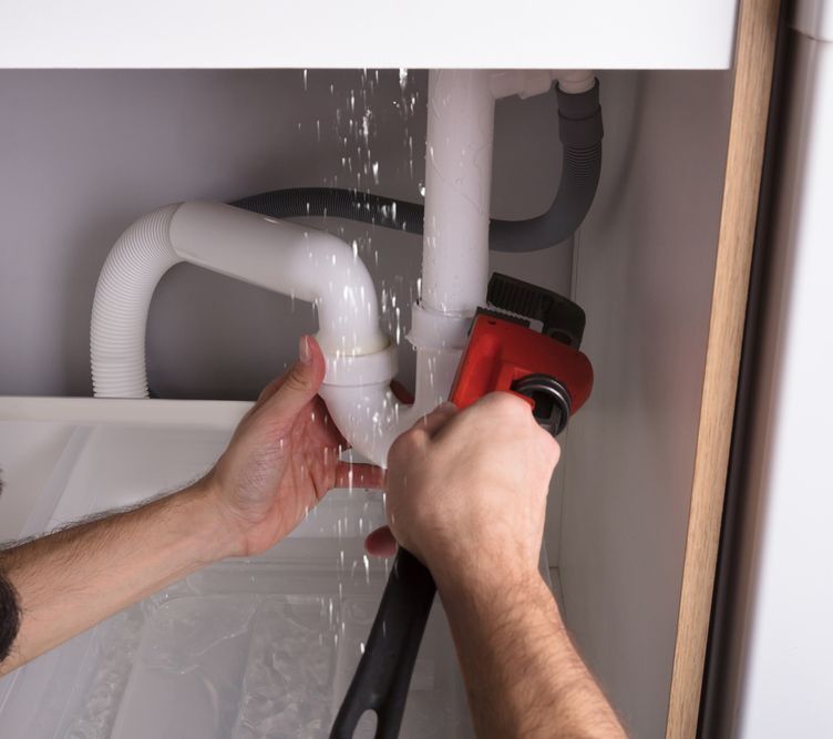 A Man Is Fixing A Sink With A Wrench — Coastal Plumbing Group in Woolgoolga, NSW