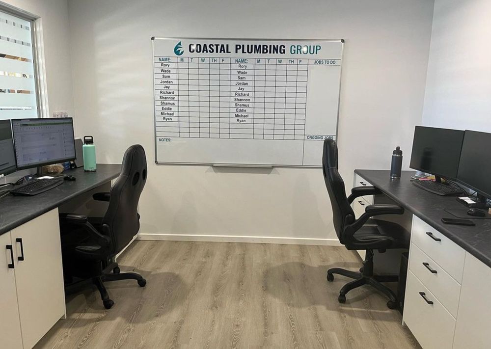 A Room With Two Desks And Two Chairs And A Whiteboard On The Wall — Coastal Plumbing Group in Woolgoolga, NSW