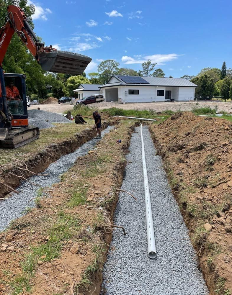 A Man Is Digging A Trench In The Dirt In Front Of A House — Coastal Plumbing Group in Woolgoolga, NSW