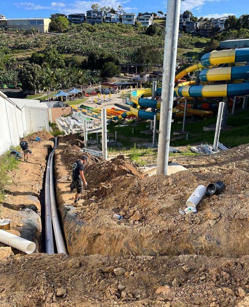 A Man Is Standing In The Dirt Next To A Water Slide — Coastal Plumbing Group in Woolgoolga, NSW