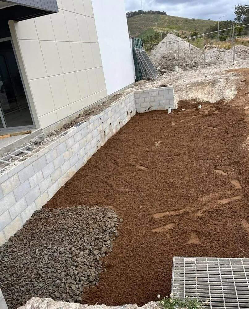 A Brick Wall Is Being Built Next To A Pile Of Dirt And Gravel — Coastal Plumbing Group in Woolgoolga, NSW