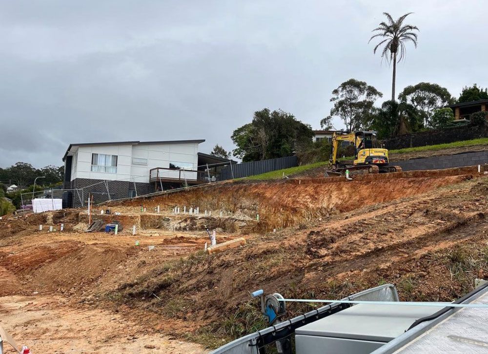 A Construction Site With A House In The Background And A Bulldozer In The Foreground — Coastal Plumbing Group in Woolgoolga, NSW