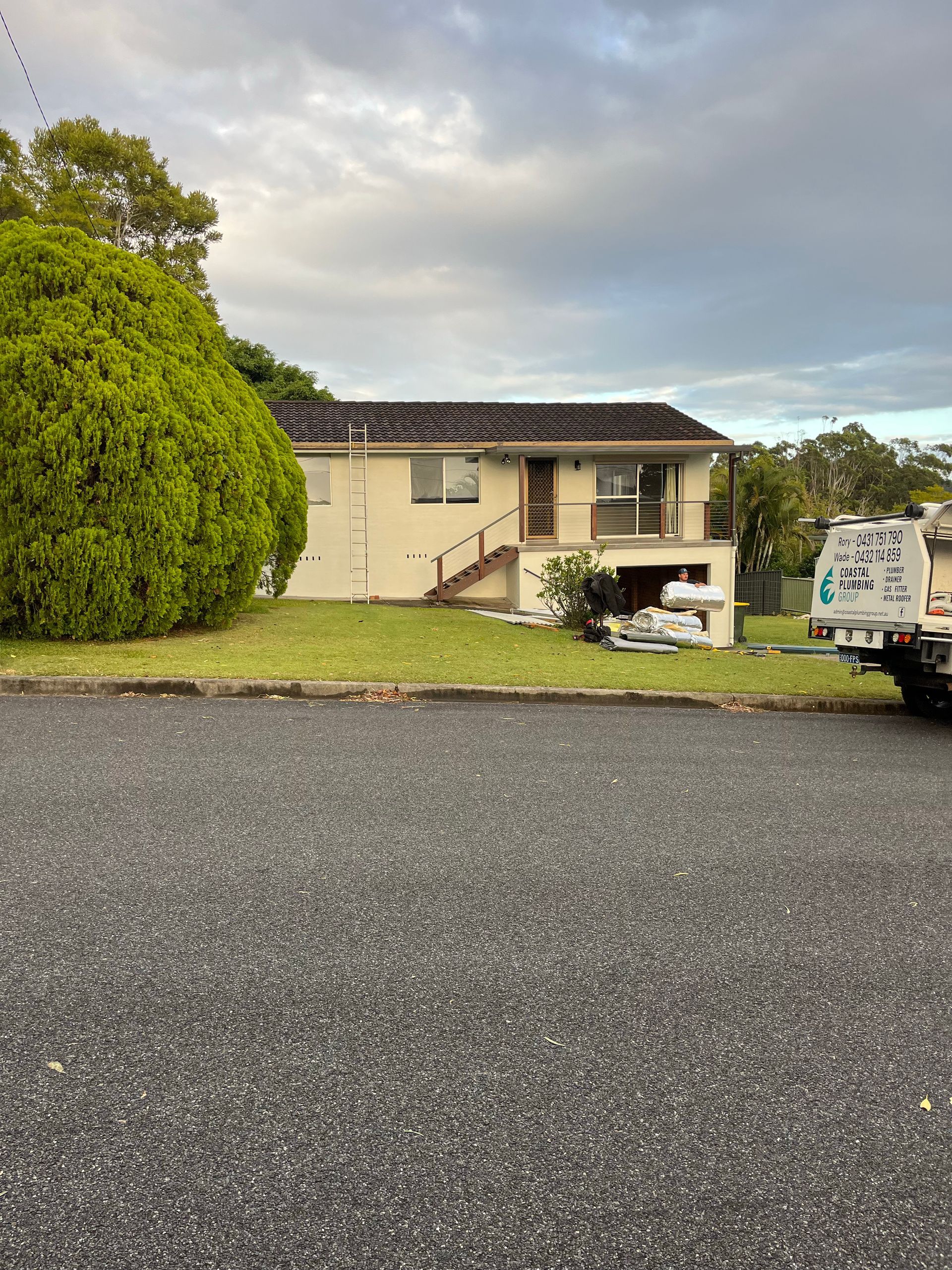A Plumber Is Working Under A Sink In A Kitchen — Coastal Plumbing Group in Woolgoolga, NSW