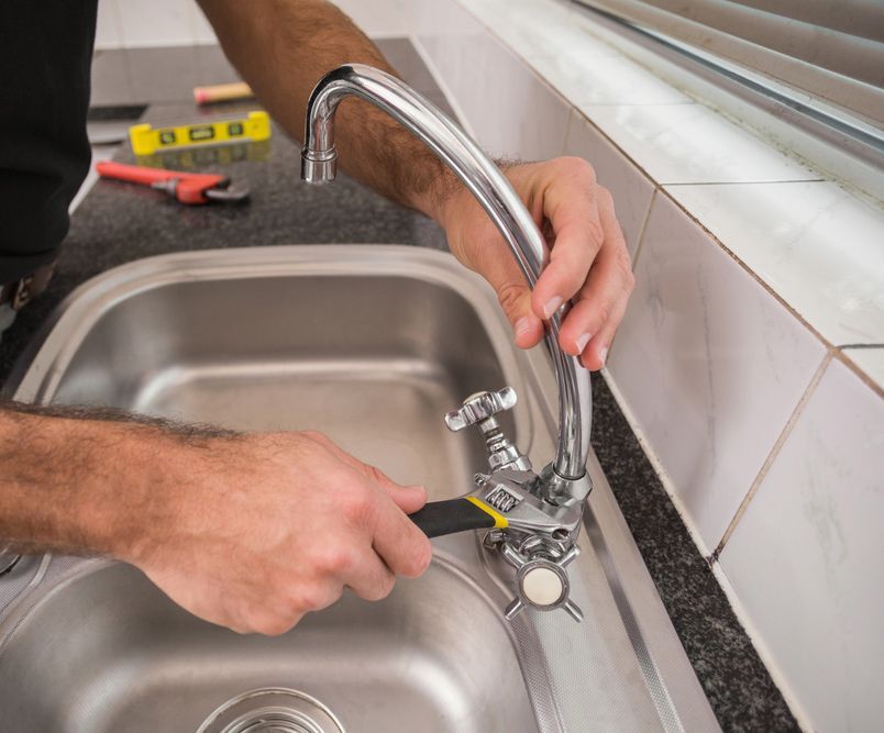 A Man Is Fixing A Sink Faucet With A Wrench — Coastal Plumbing Group in Woolgoolga, NSW