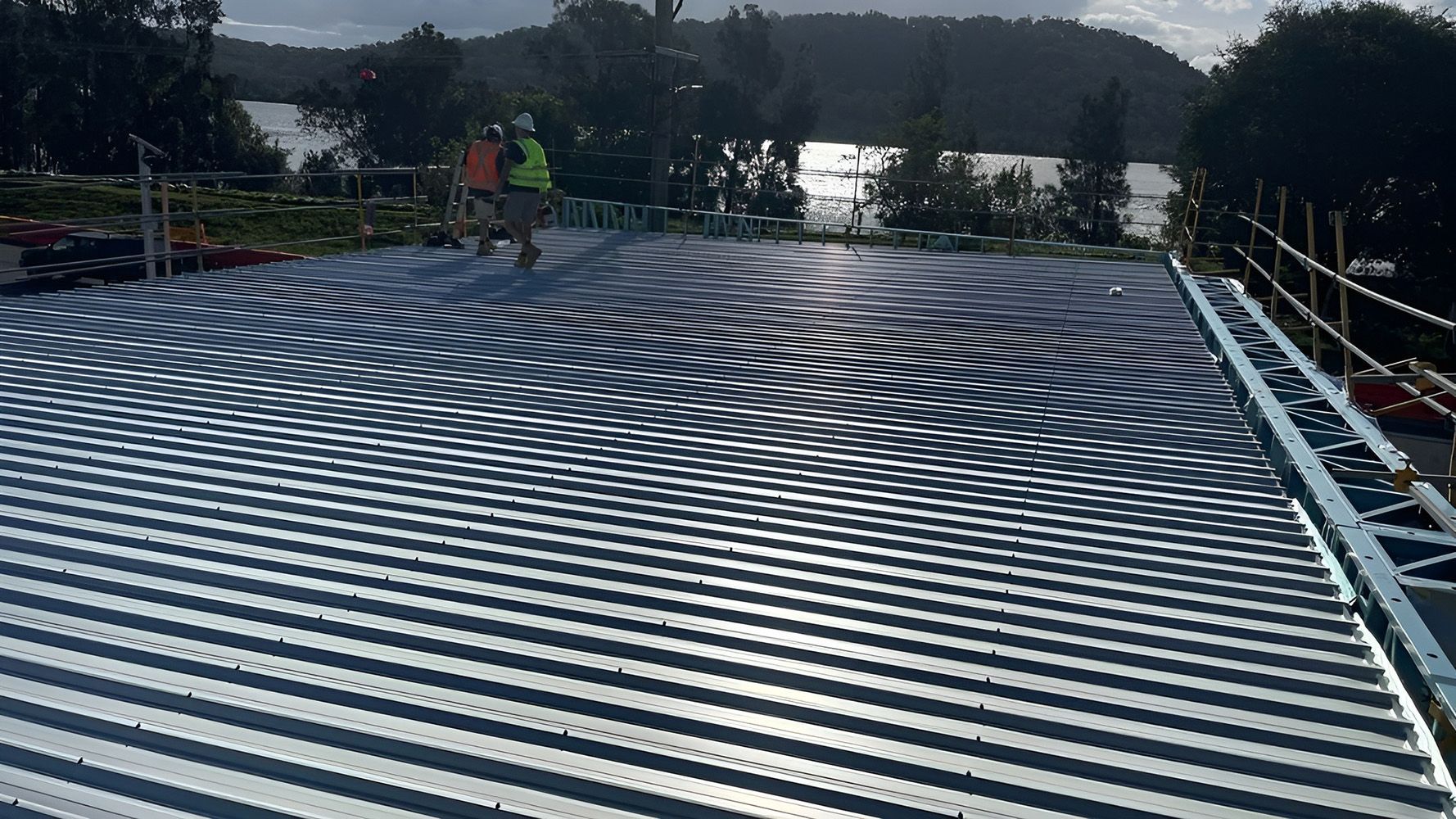 Two Construction Workers Stand On A Metal Roof — Roof Repairs Coffs Harbour -Coastal Plumbing Group in Woolgoolga, NSW