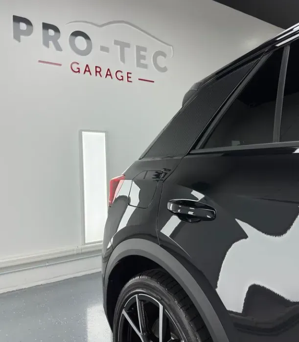 A black car is parked in a pro-tec garage with a quality window tint completed.