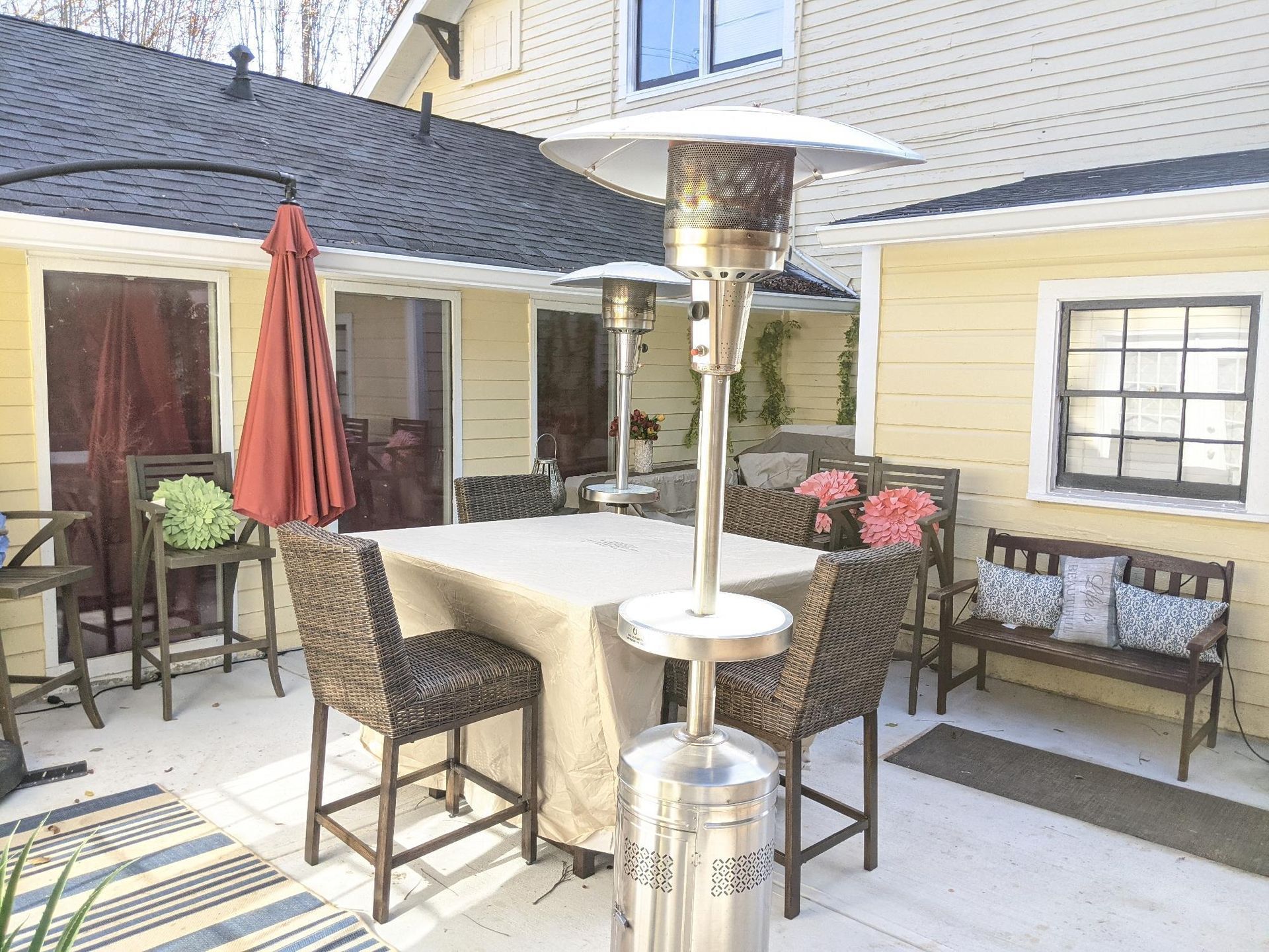 Patio with wicker seating, umbrella tables, and a standing heater in a small courtyard.