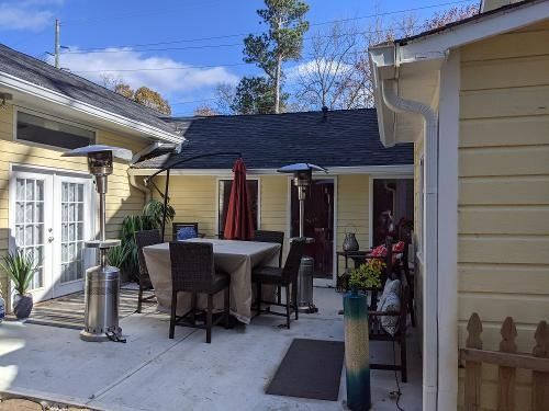 Patio with outdoor dining table, chairs, umbrellas, and potted plants beside a house in daylight