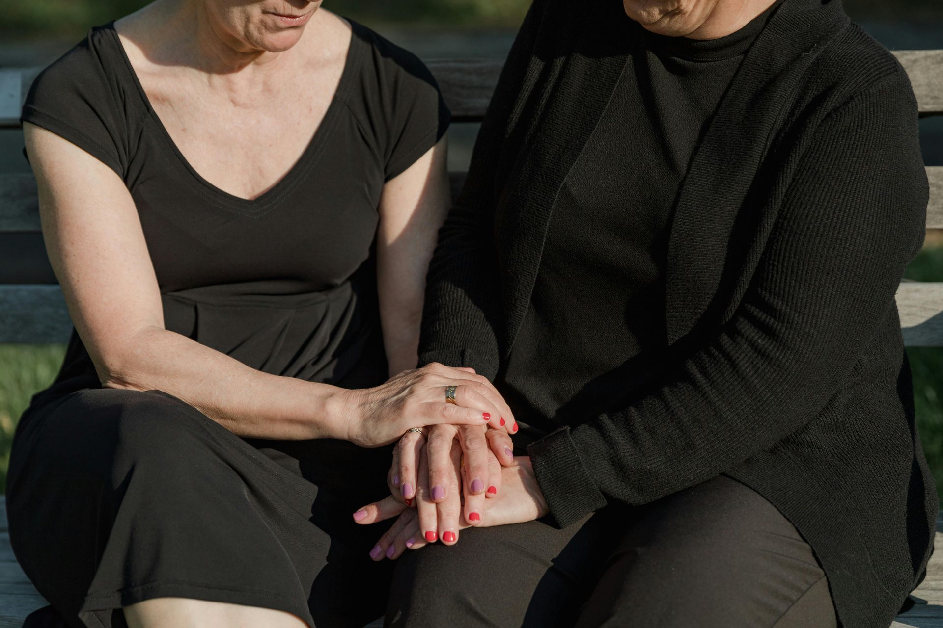 Two seated people holding hands, one in a black dress and the other in a black sweater and pants.