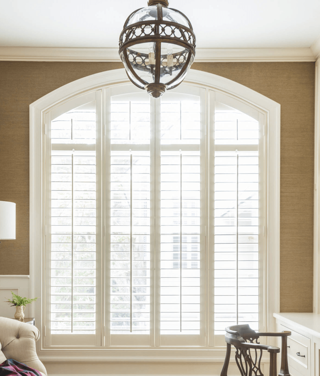 Arched White Wood Plantation Shutters with divider rail in living room window.