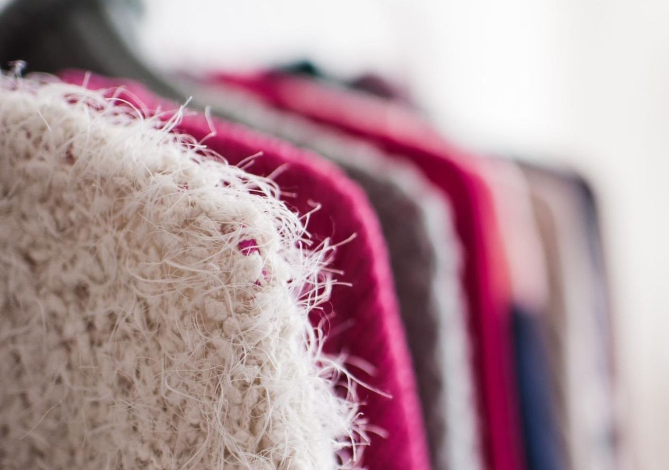 A close up of a sweater hanging on a rack in a closet.