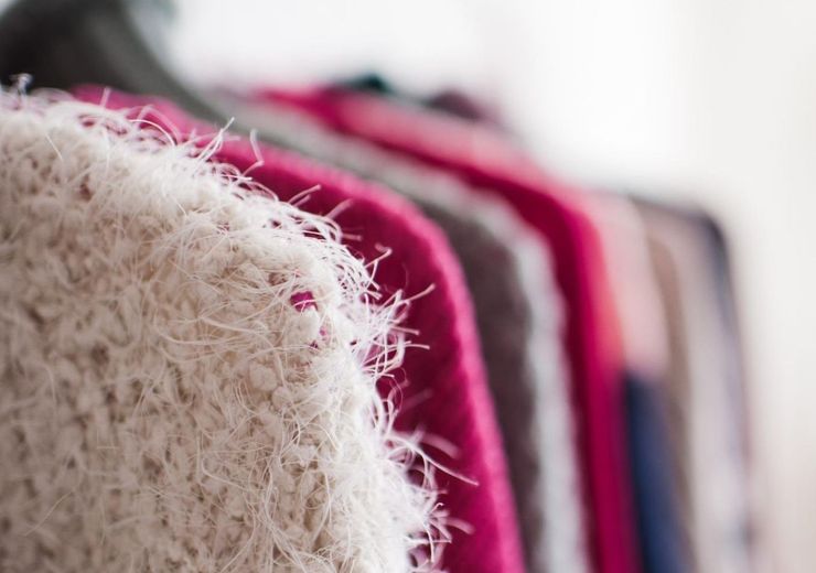 A close up of a sweater hanging on a rack in a closet.