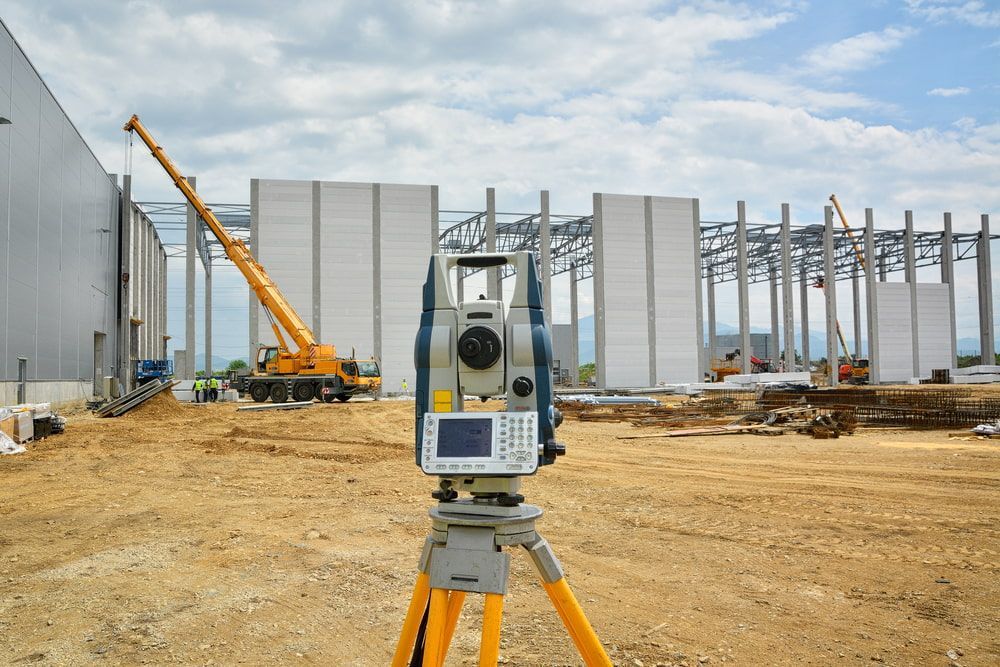 A Total Station Is Sitting On A Tripod In Front Of A Large Building Under Construction  — CalCo Surveyors Pty Ltd in Gloucester, NSW