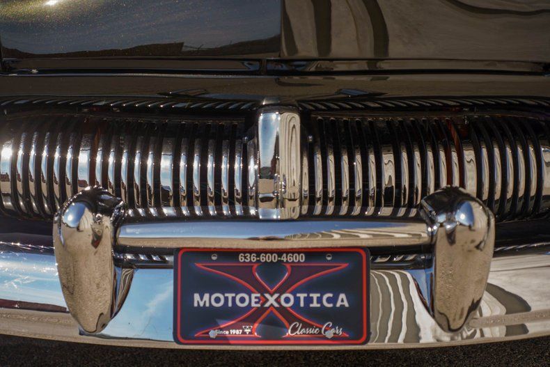 Close-up of a classic car's chrome grill and front bumper with a MotoeXotica dealership license plate.