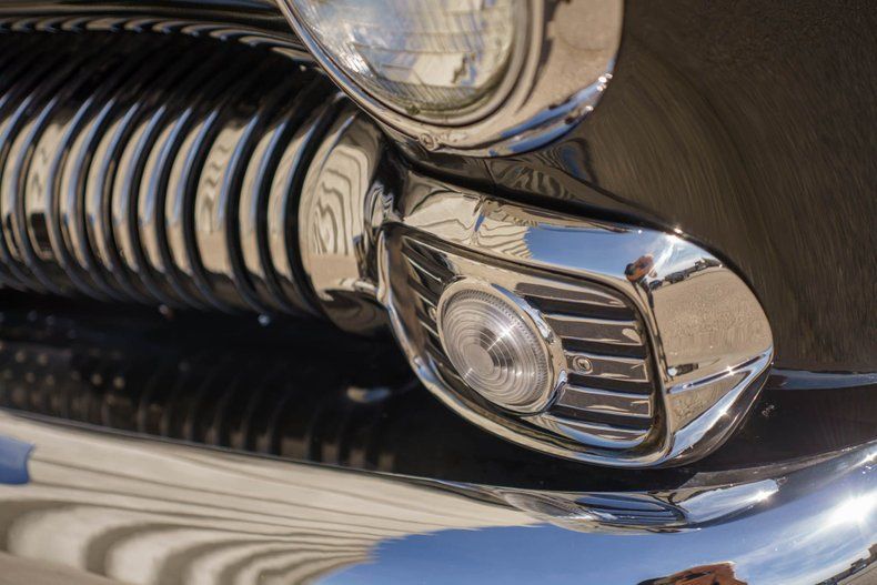 Close-up view of the chrome front grille, headlight, and turn signal of a vintage classic car.