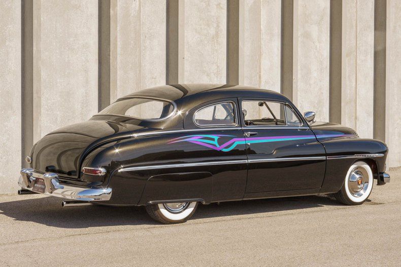 A customized black vintage car with blue and purple graphic accents parked in front of a gray, vertically striped wall.