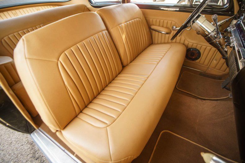Car interior showing tan leather bench seats, steering wheel, and dark brown carpeting.