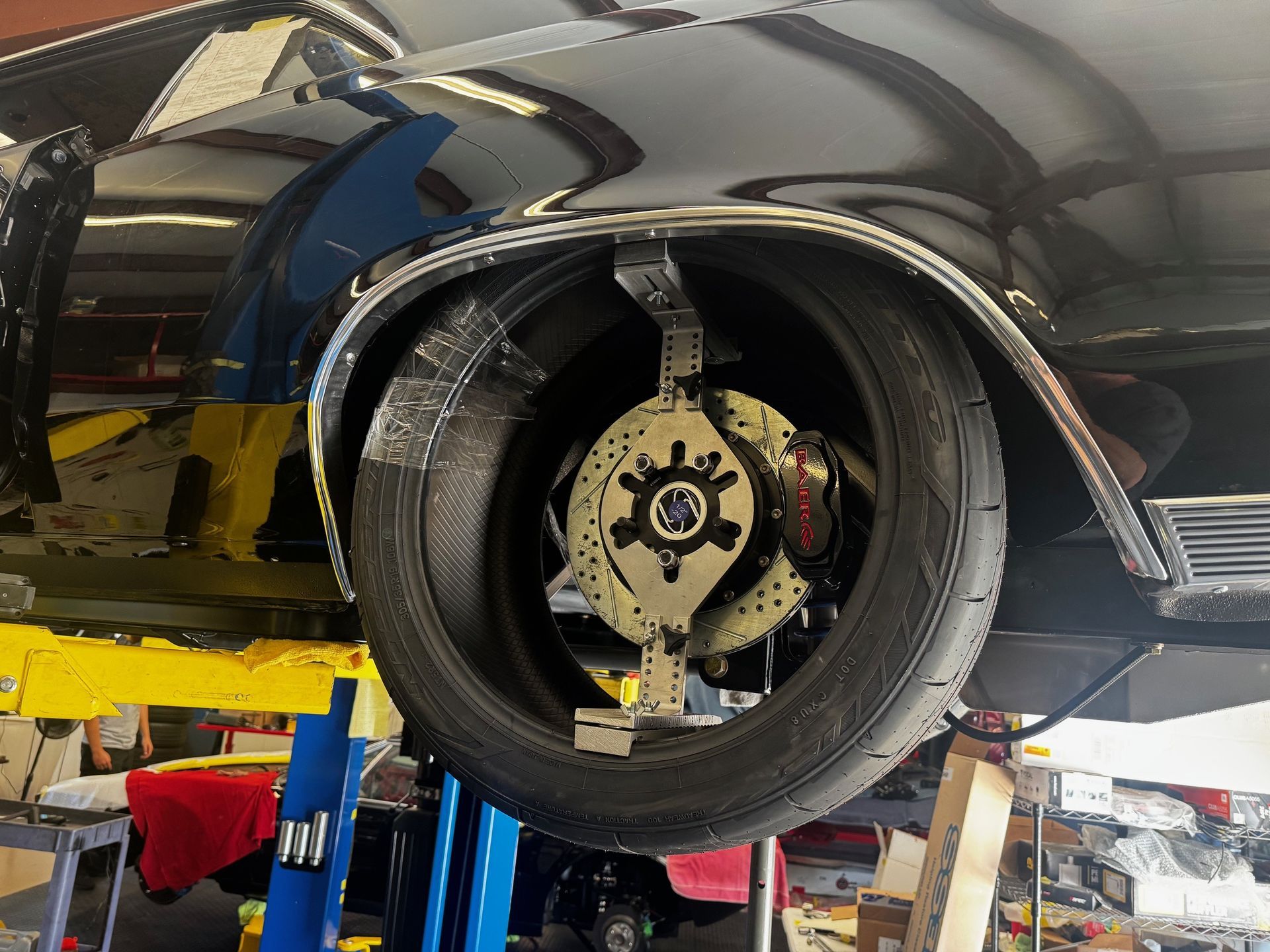 A car wheel is being measured for fitment using a metal adjustment tool while mounted on an automotive lift.