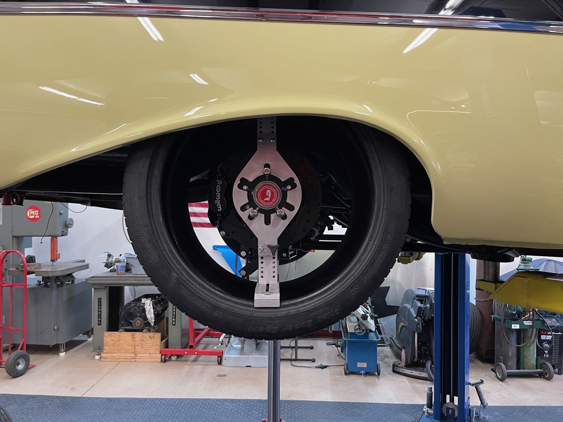 A yellow car lifted on a garage hoist with a wheel alignment tool attached to the tire.