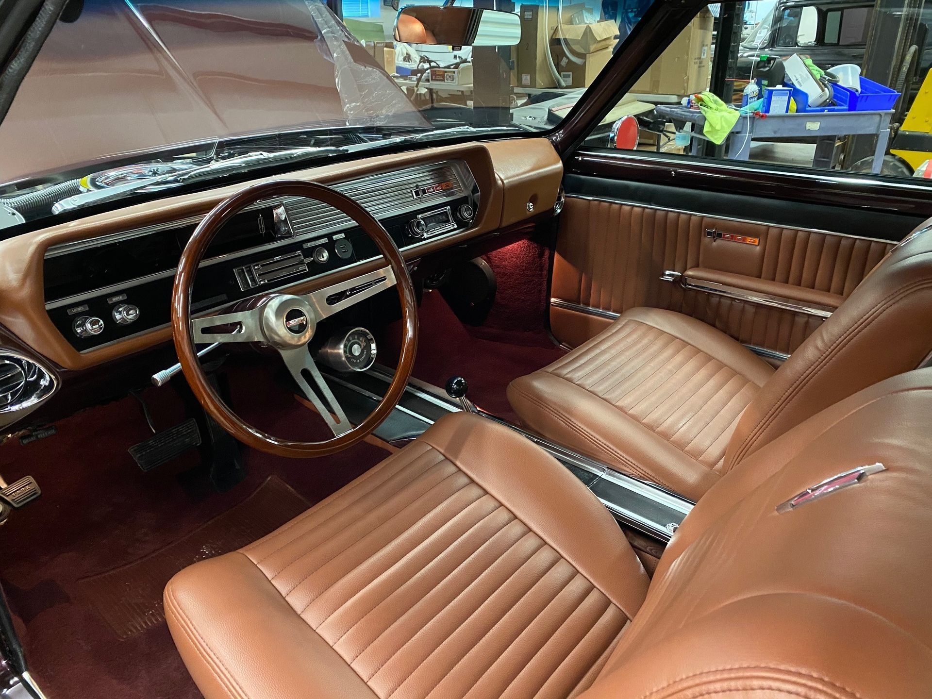 Tan leather interior of a classic car with bucket seats, a wooden steering wheel, and a maroon carpeted floor.
