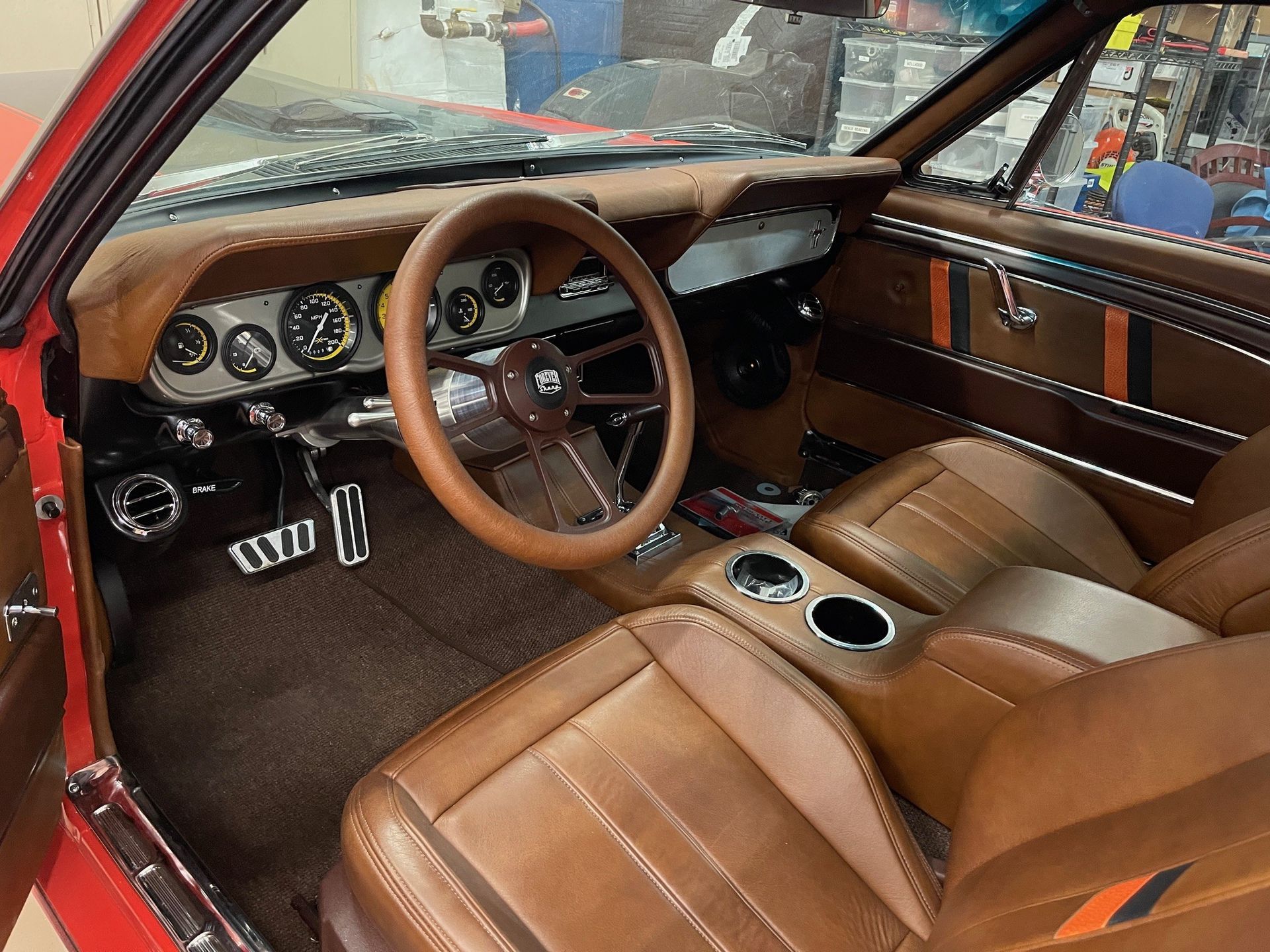 The interior of a classic car featuring tan leather upholstery, a matching steering wheel, and a brushed metal dashboard.