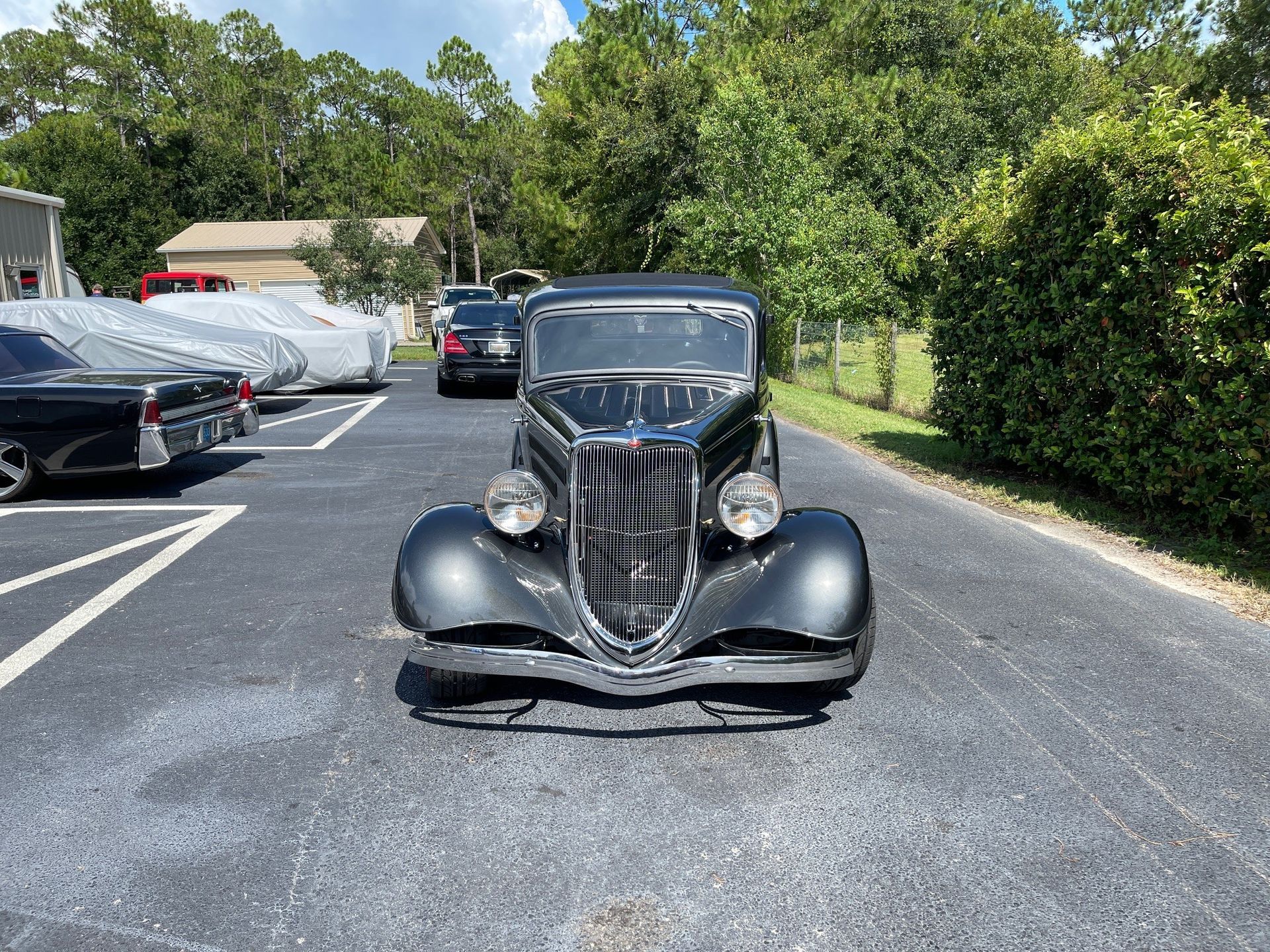 A dark-colored, vintage 1934 Ford sedan parked in an asphalt lot on a sunny day.