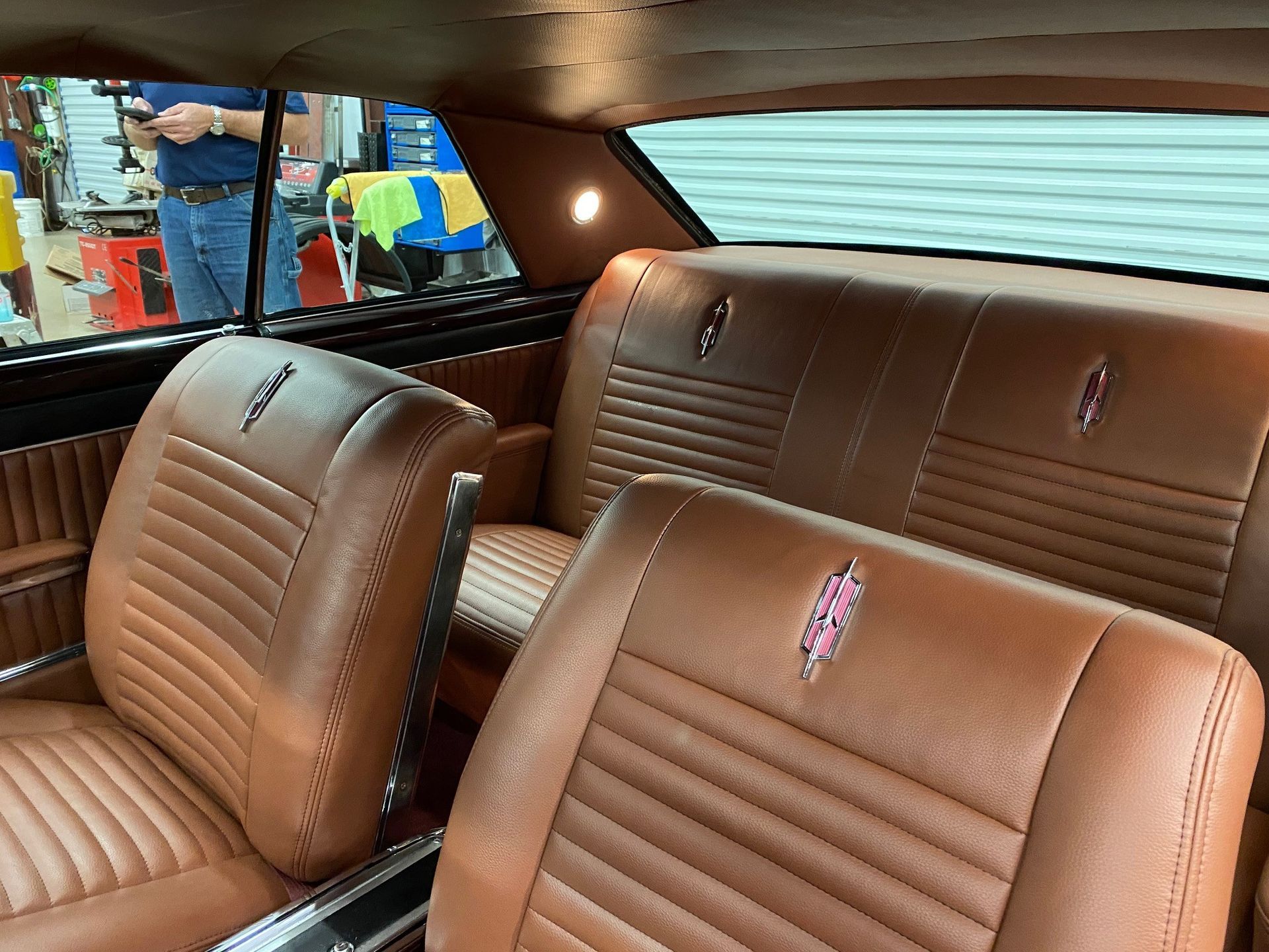 The interior of a classic car featuring tan vinyl bucket seats, a matching bench seat, and a small illuminated ceiling lamp.