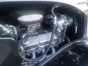 A clean, chrome-accented V8 engine inside the engine bay of a classic vintage car.