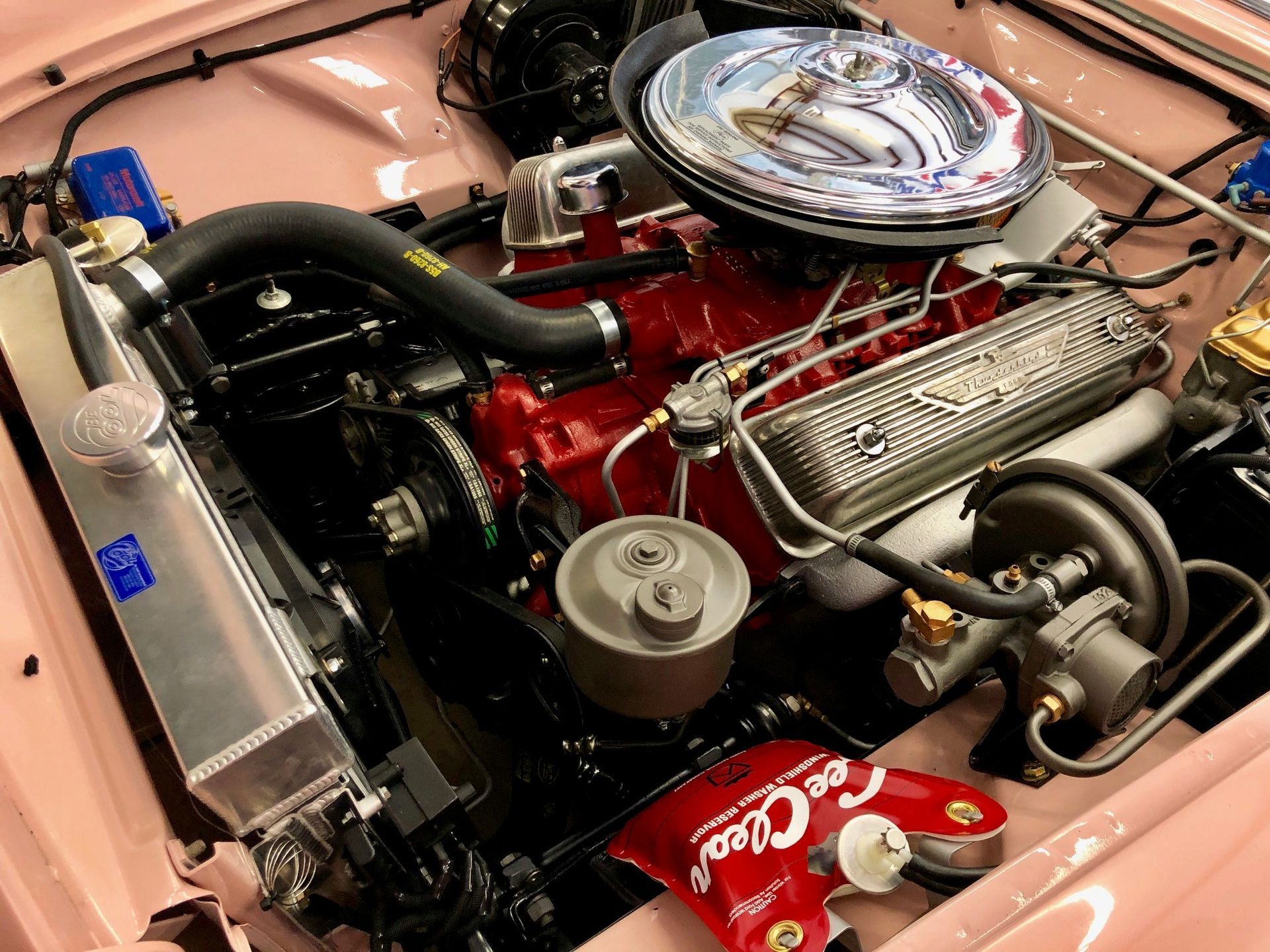 A close-up of a clean car engine bay with a bright red block, a chrome air cleaner, and a polished aluminum radiator.
