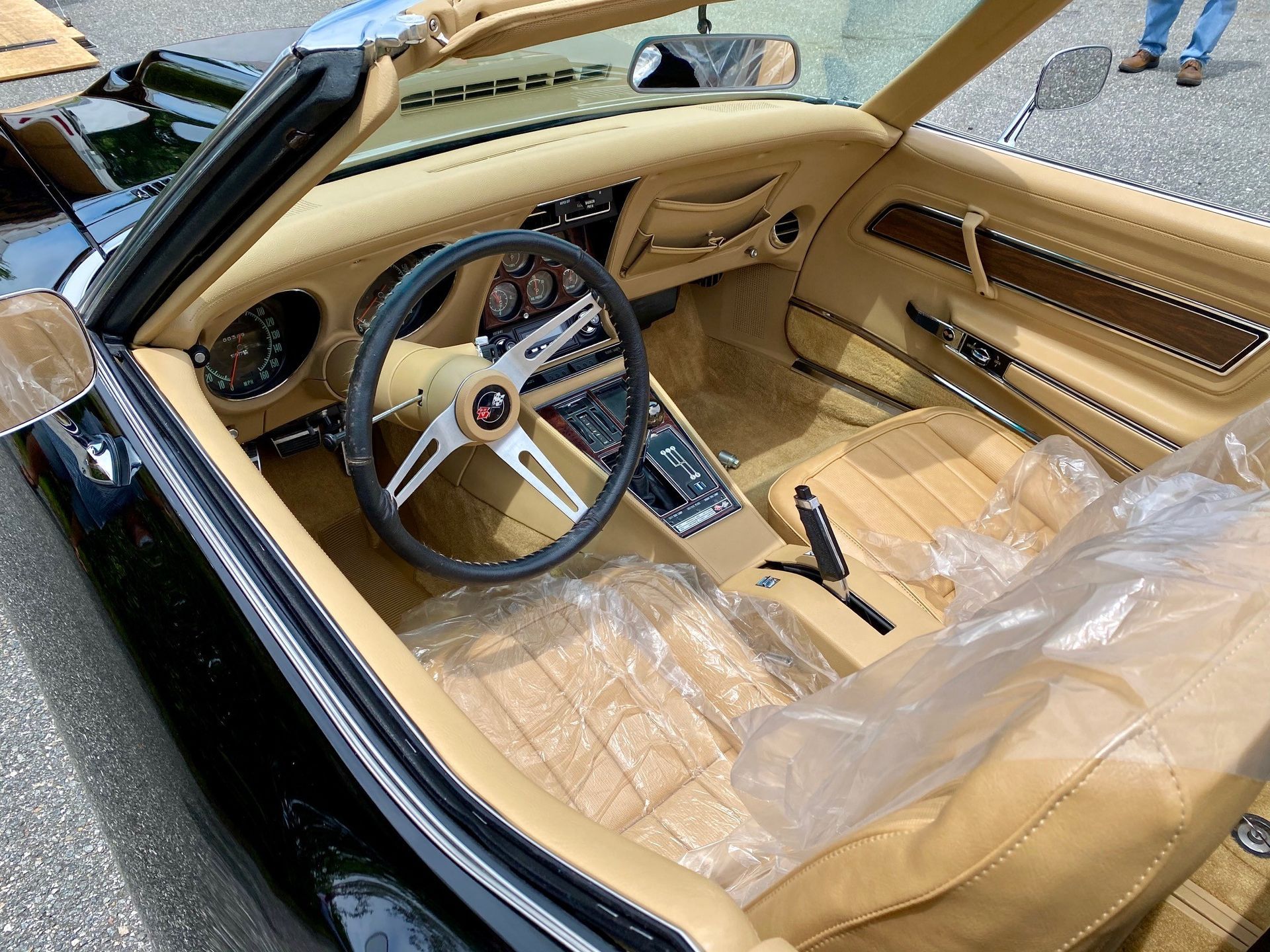 High-angle view of a classic black convertible car interior with tan leather seats covered in protective plastic.