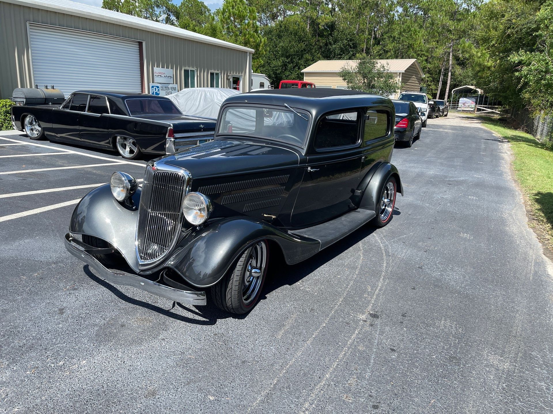 A black vintage car parked on an asphalt lot in front of a metal warehouse building.