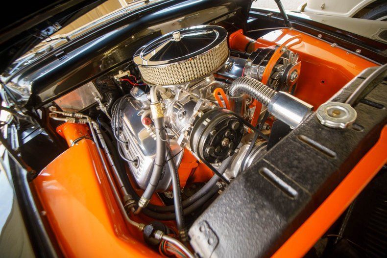 A high-angle view of a clean, modified car engine with orange interior housing, a chrome air filter, and black accents.