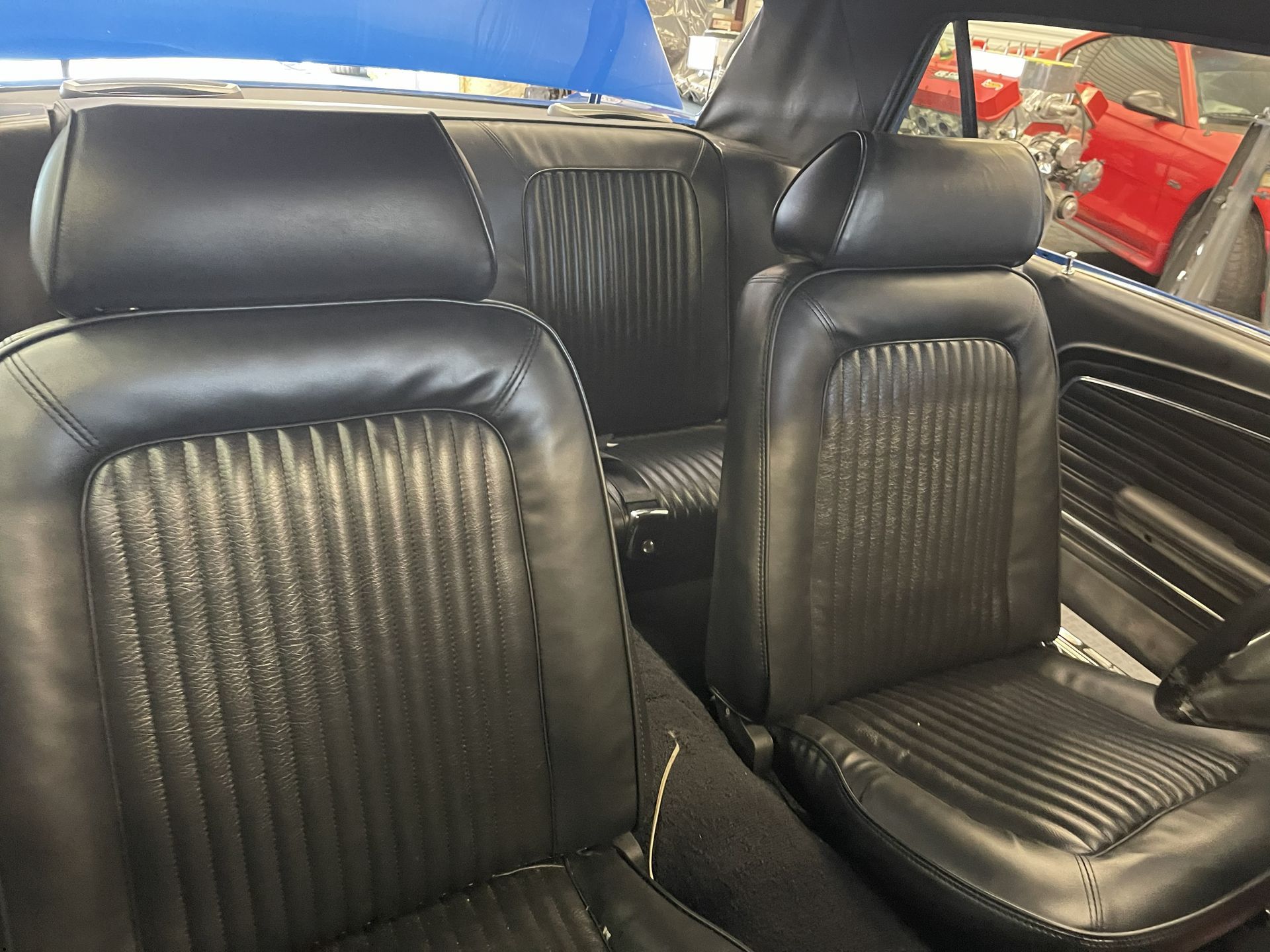 Black leather bucket seats inside a classic car with vertical pleats and headrests.