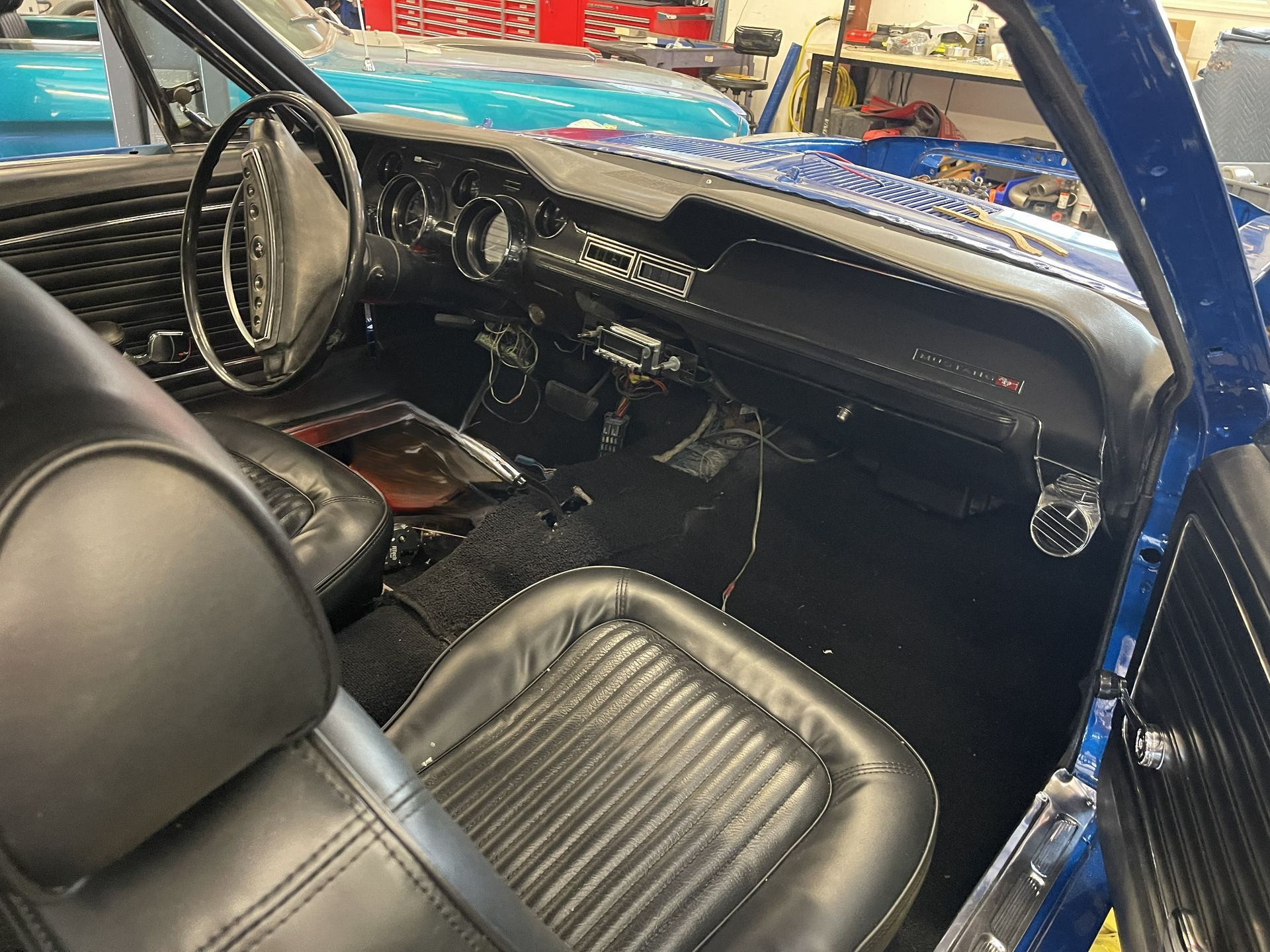 Interior of a blue vintage car featuring black leather seats, a classic steering wheel, and a black dashboard.