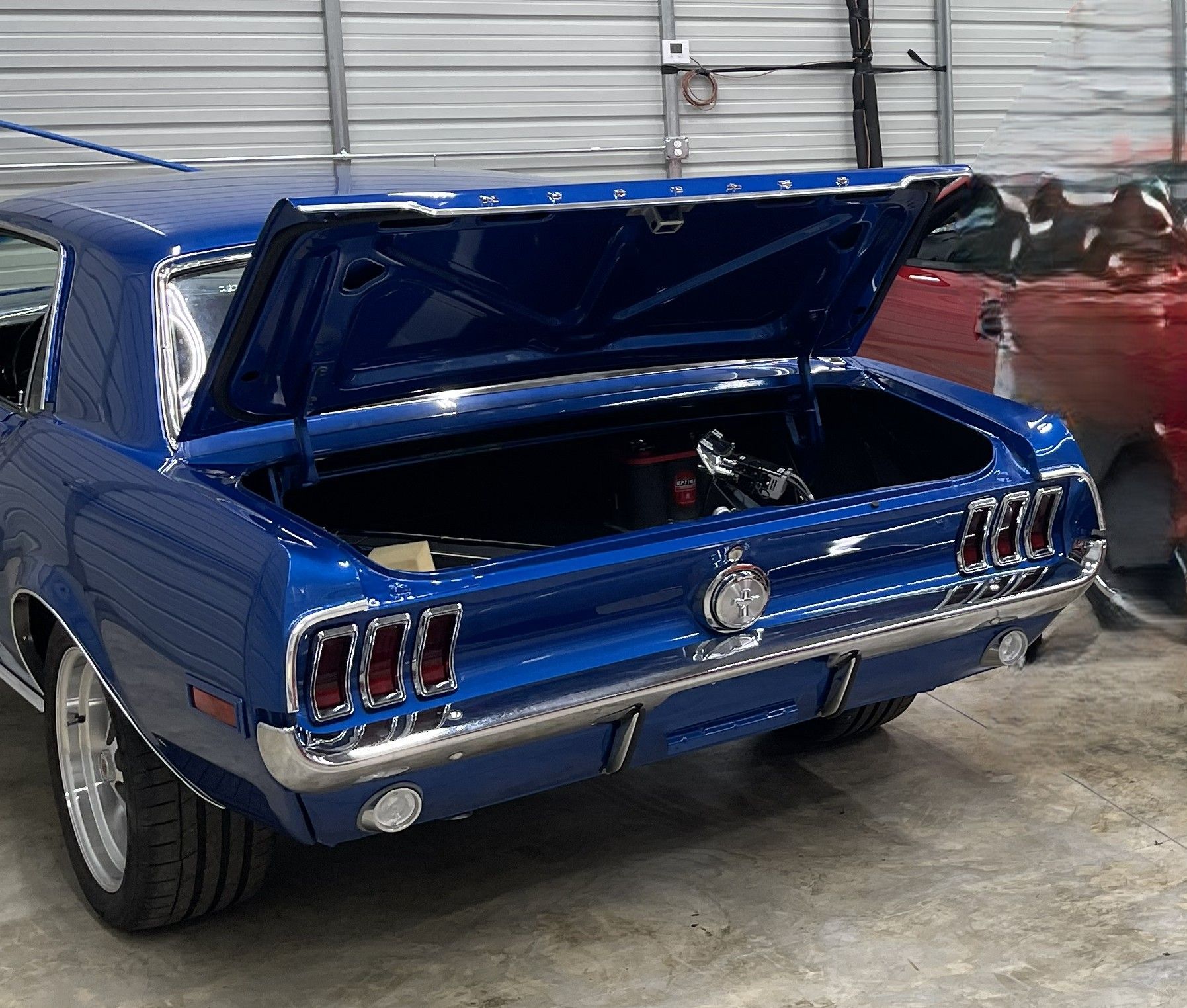 Rear view of a bright blue 1967-1968 Ford Mustang with an open trunk in a garage.