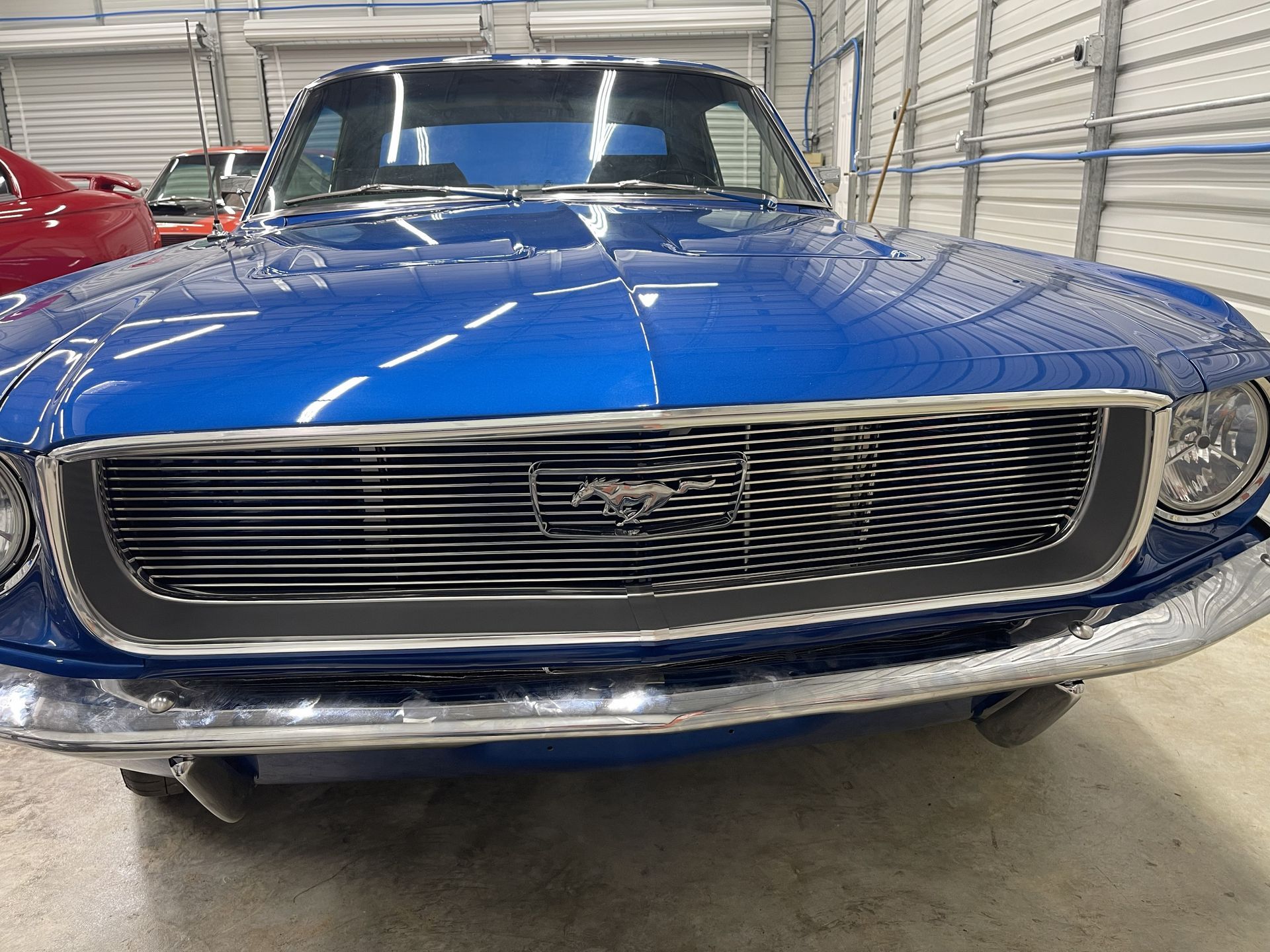 Front view of a bright blue vintage Ford Mustang parked inside a garage with its chrome bumper and grille visible.
