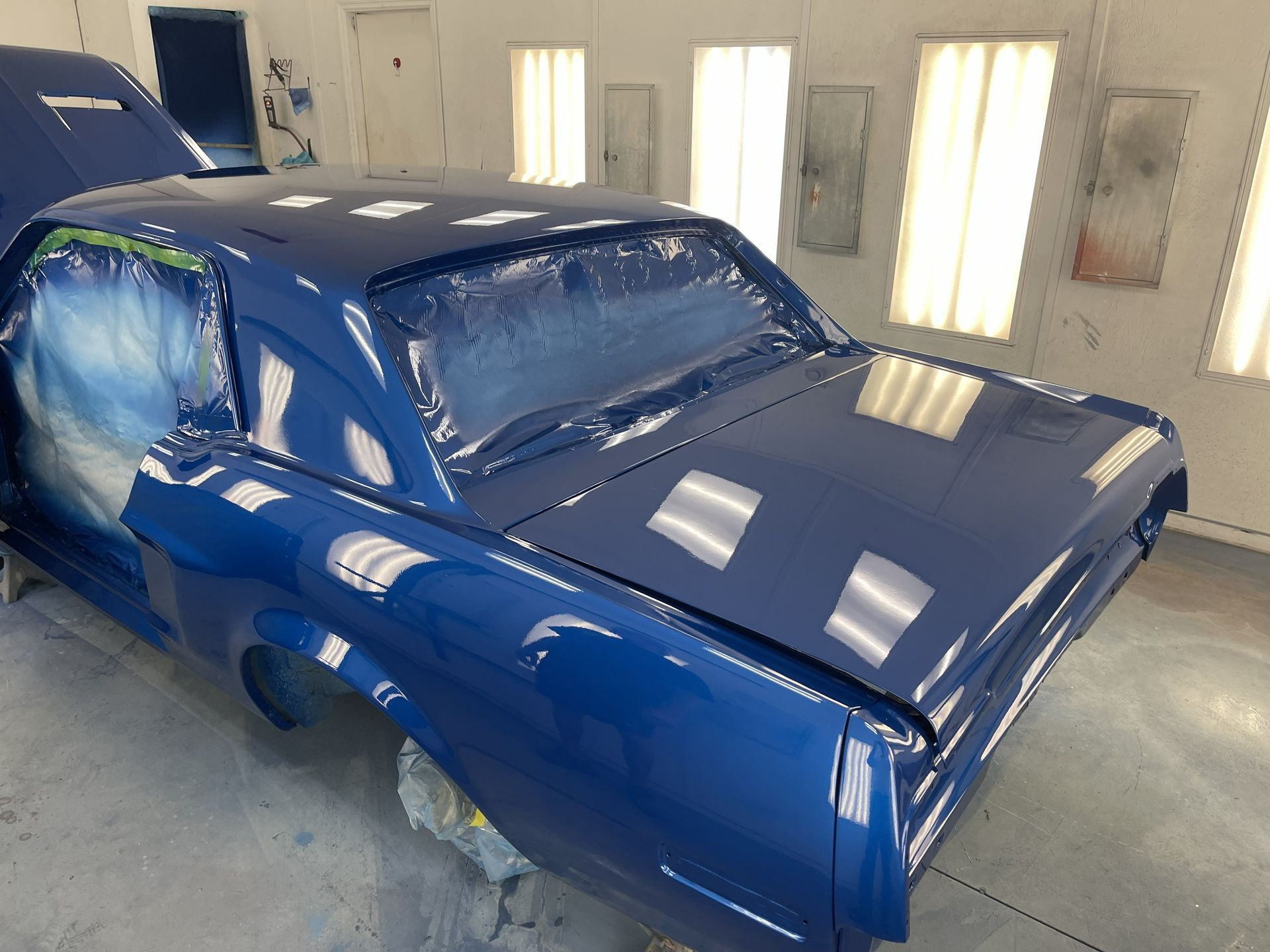 A shiny dark blue classic car inside a professional automotive paint booth.