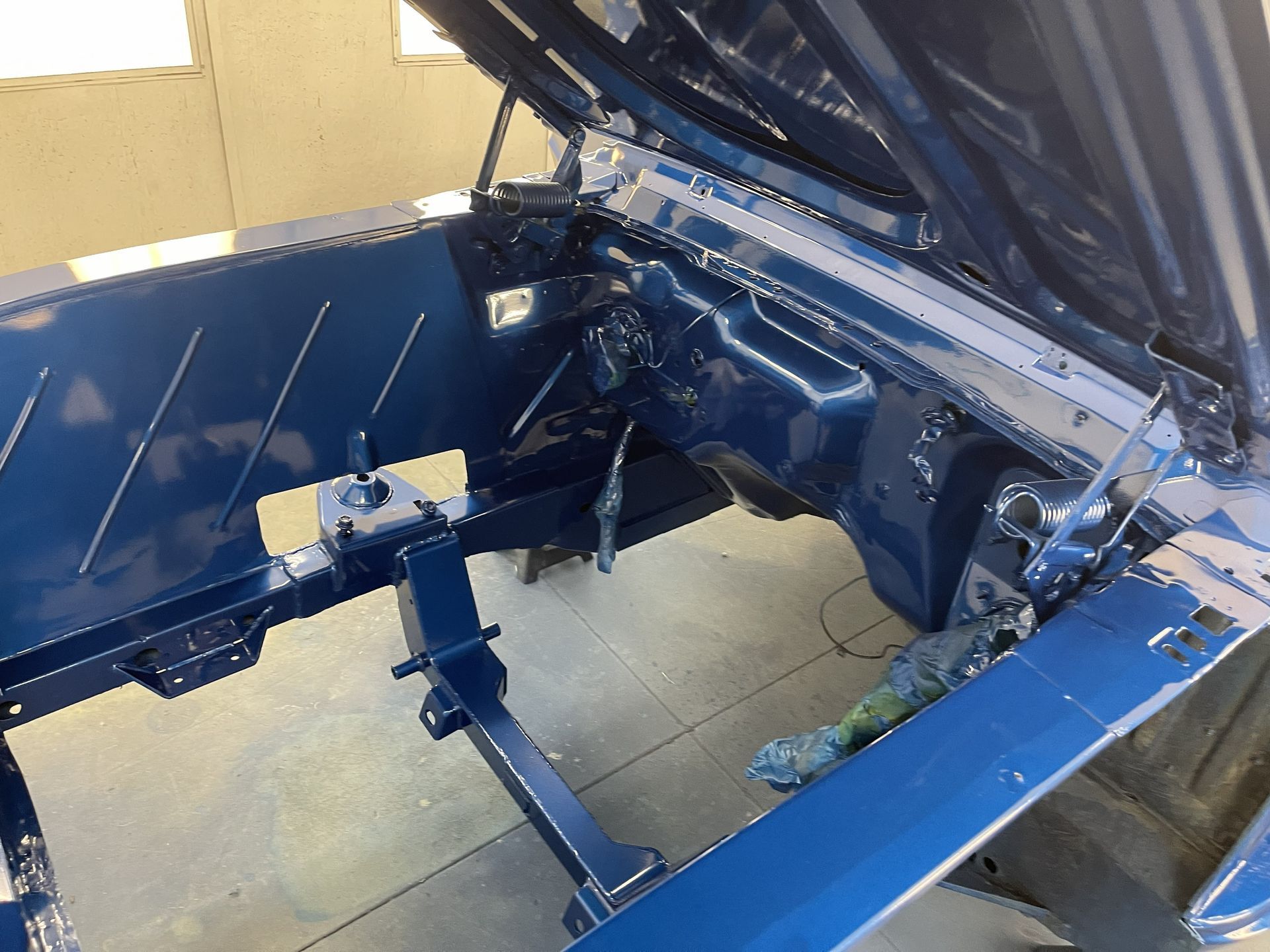 A freshly painted deep blue classic car engine bay with an open hood inside a workshop.