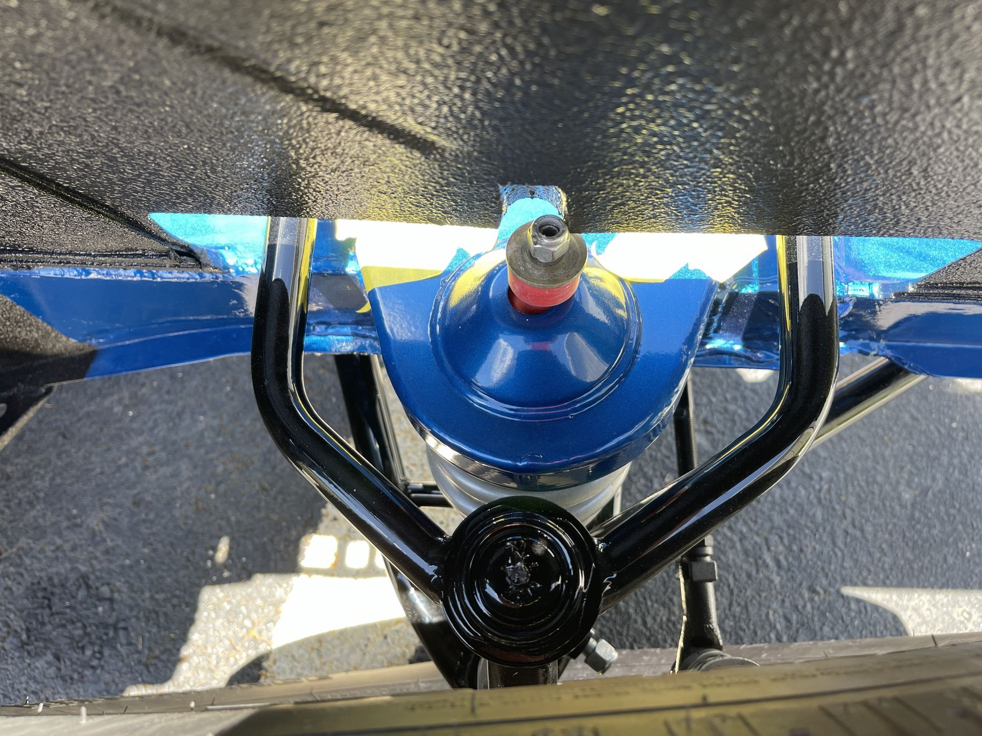 Close-up, top-down view of a vehicle's black metal A-arm suspension component mounted over a bright blue spring housing.