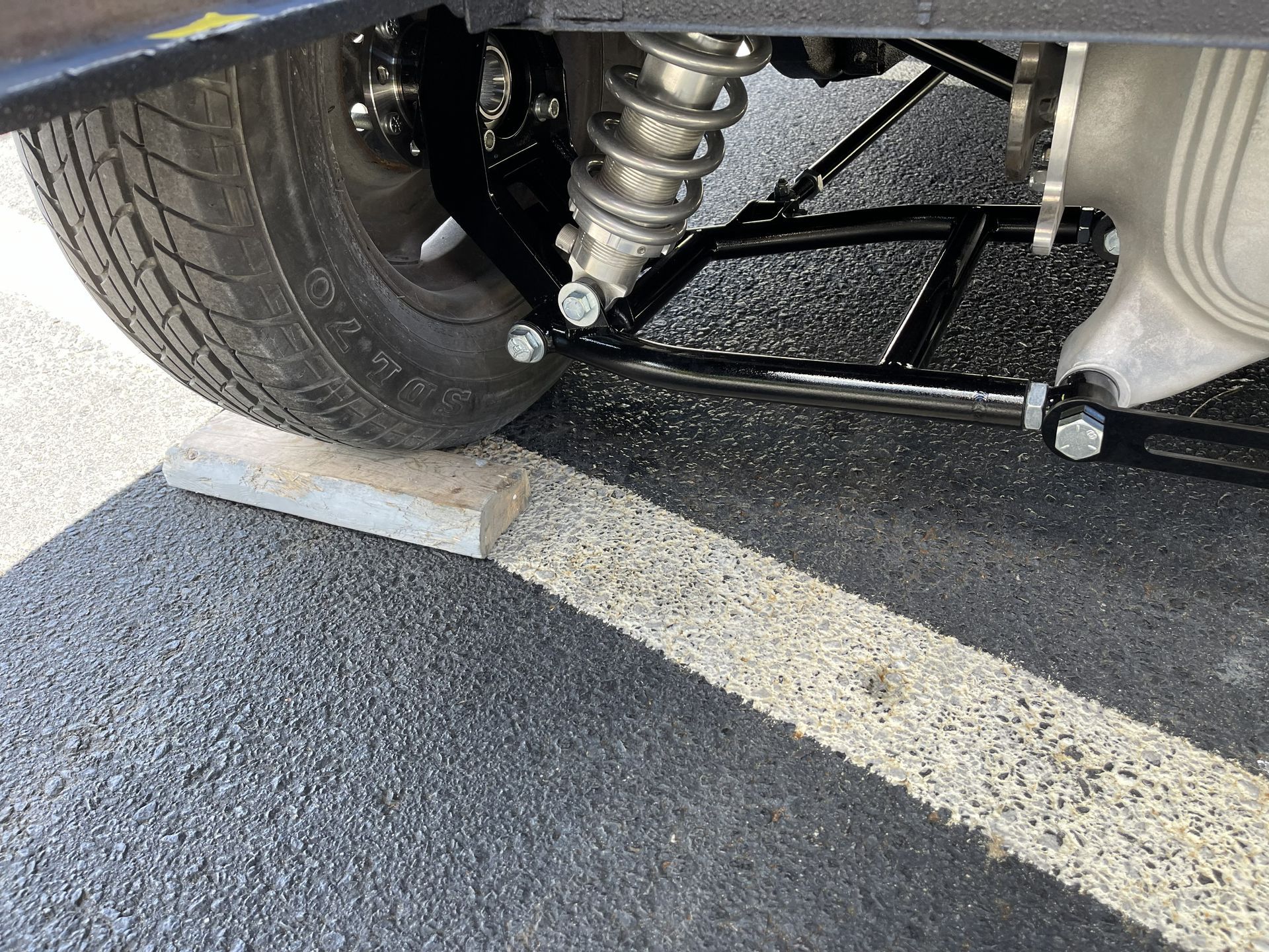 A close-up view of a vehicle's rear suspension, featuring a silver coilover shock absorber attached to a black metal frame.