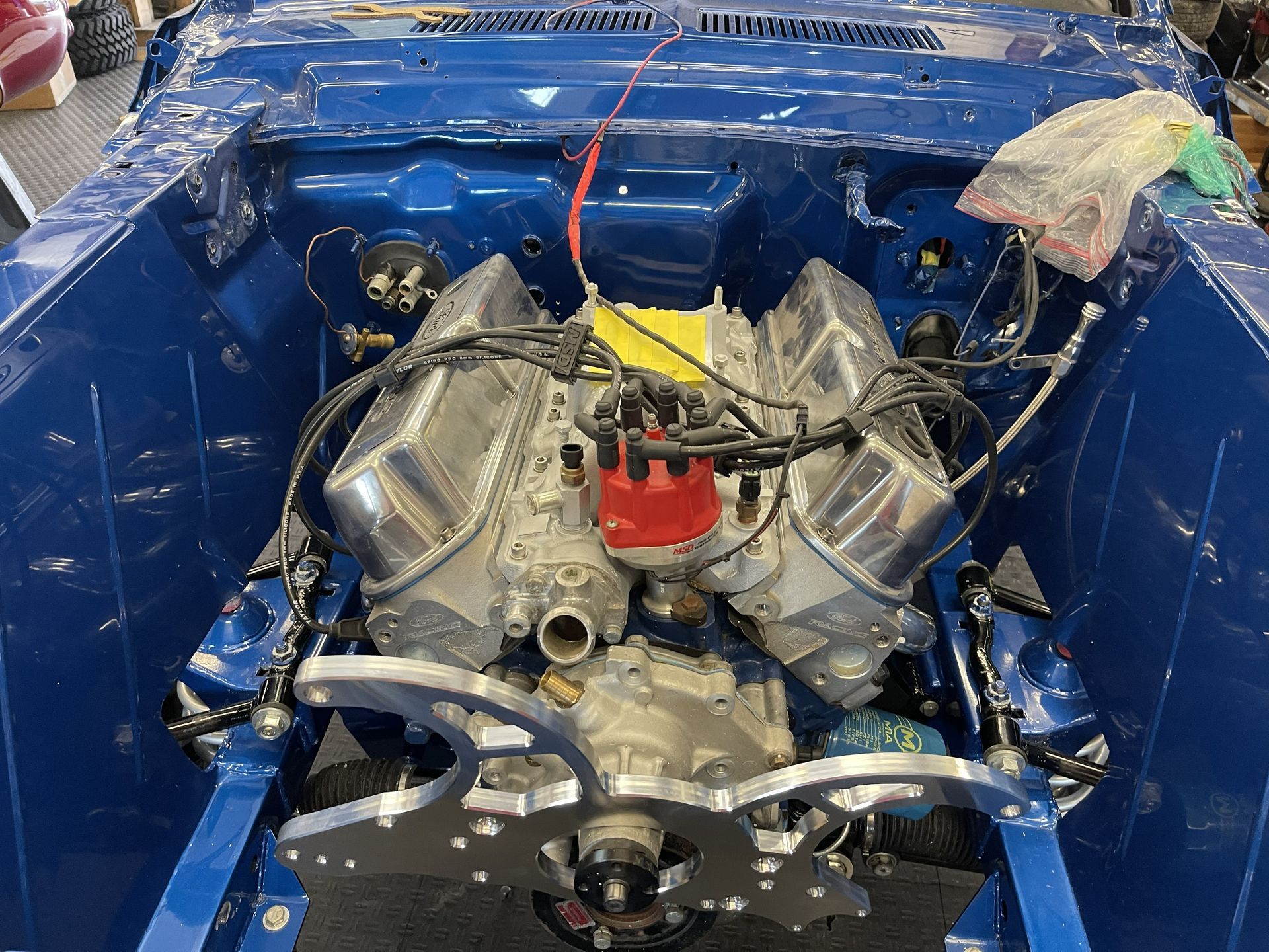 A V8 engine with chrome valve covers and a red distributor cap installed in a bright blue, freshly painted car engine bay.