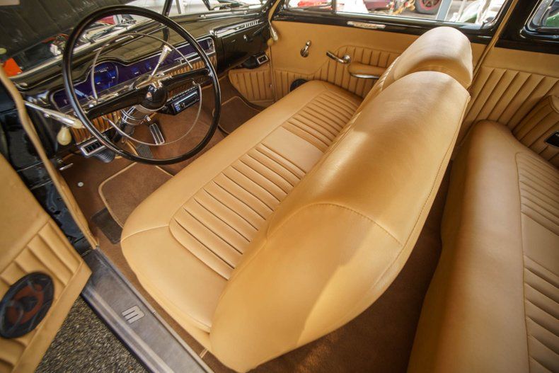 Interior view of a classic car with tan leather bench seating and a large steering wheel over a dark dashboard.