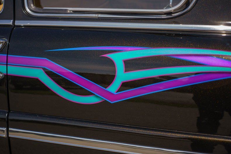 A close-up of a black car door featuring stylized, geometric pinstripe decals in vibrant purple and teal.