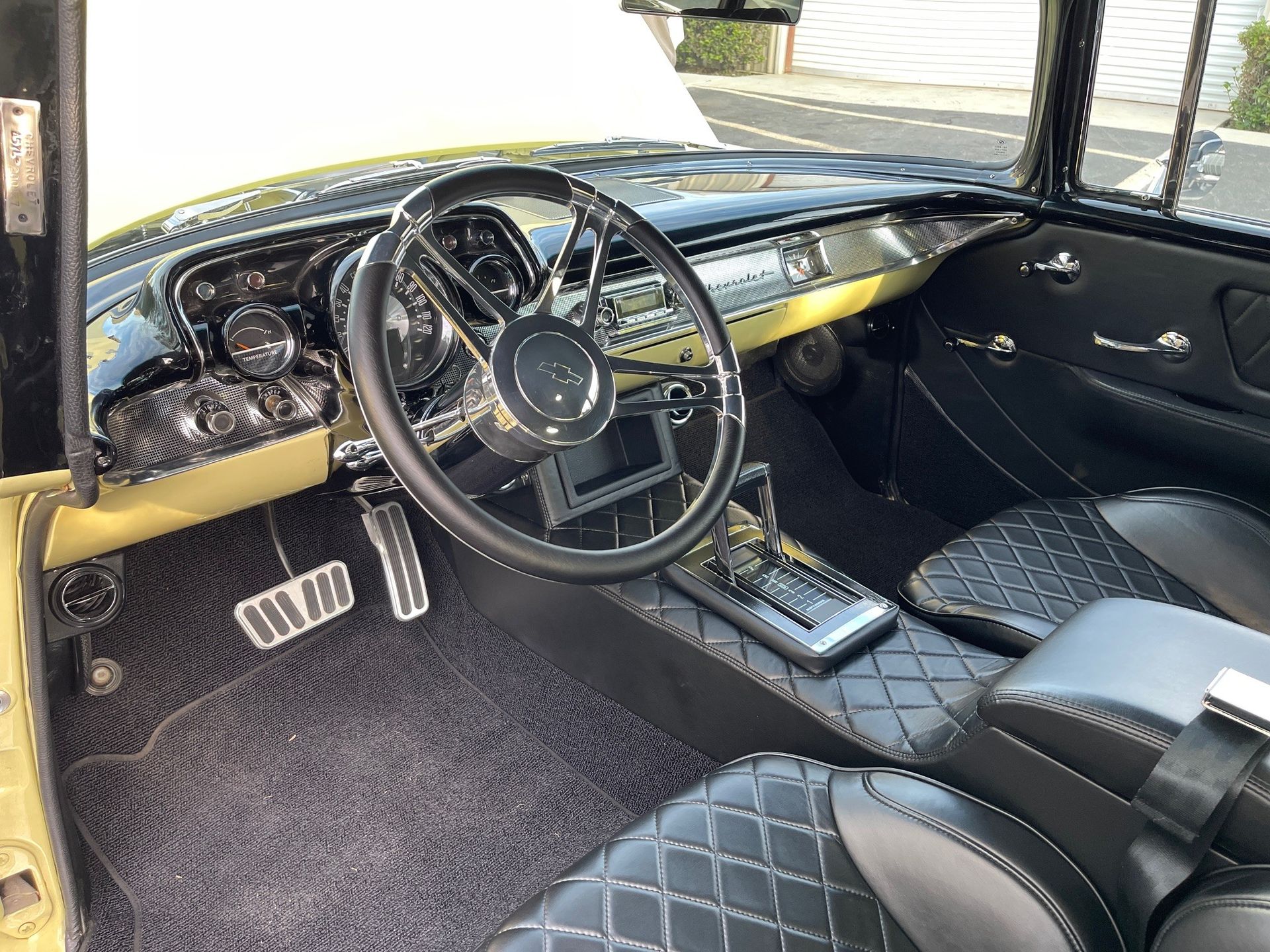 Interior view of a classic car with a custom black diamond-stitched upholstery, yellow dashboard, and modern pedals.