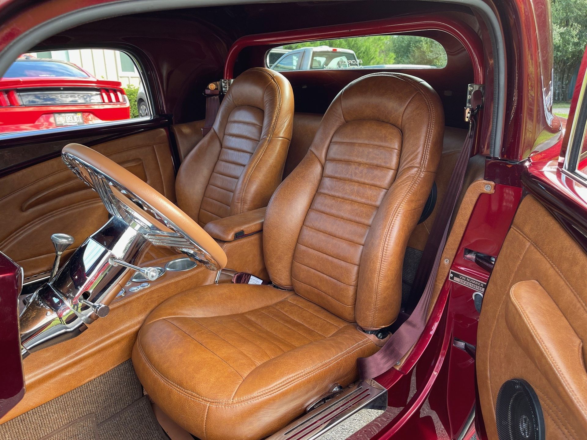 Interior of a customized vintage car featuring tan leather bucket seats, a chrome steering column, and maroon trim.