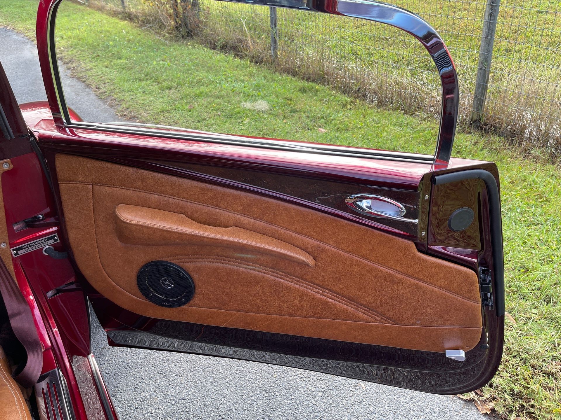Open door of a dark red car with tan textured upholstery and a circular speaker, viewed from the exterior.