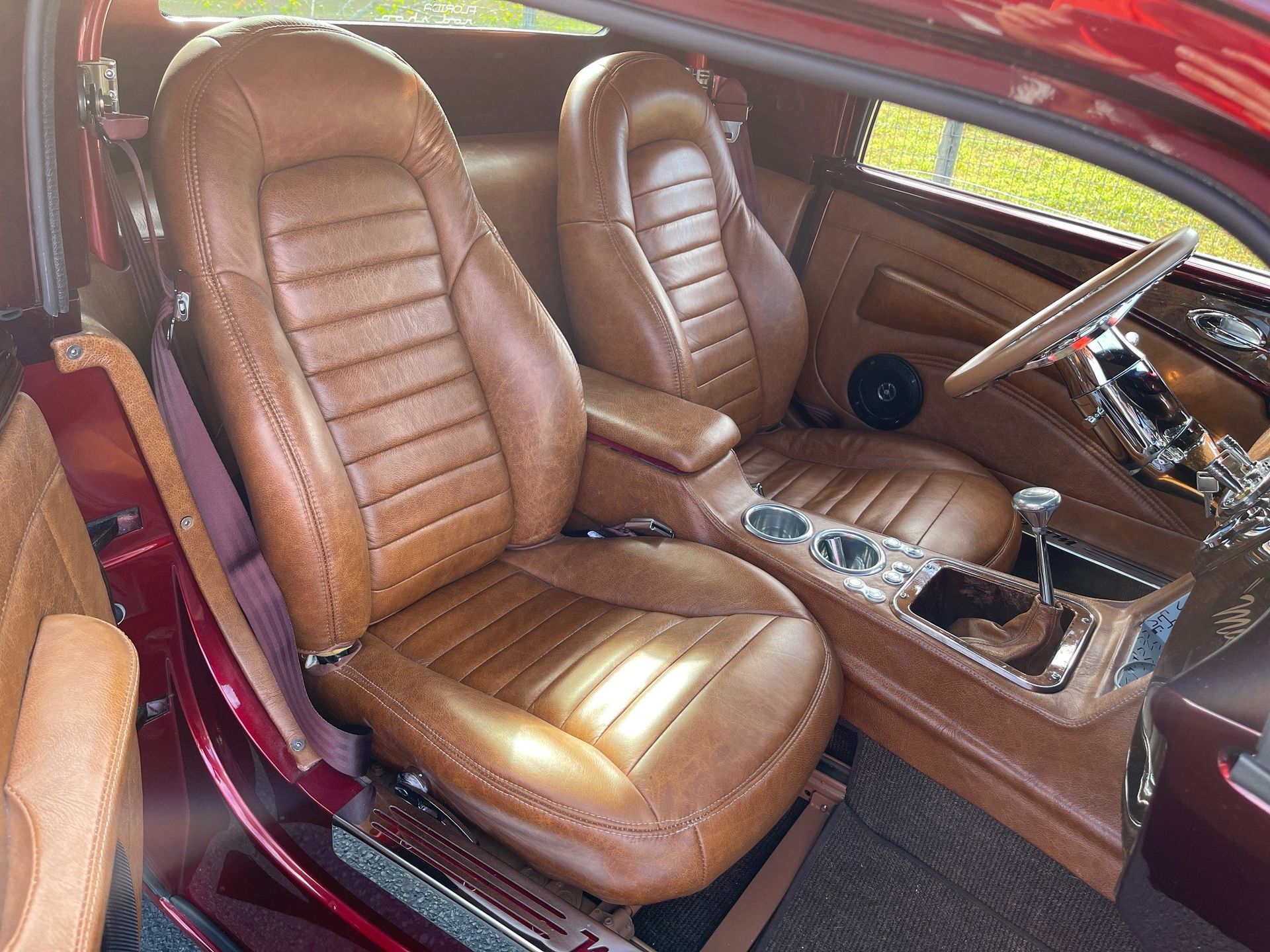 The interior of a classic car featuring two tan, horizontally-stitched leather bucket seats and a matching dashboard.