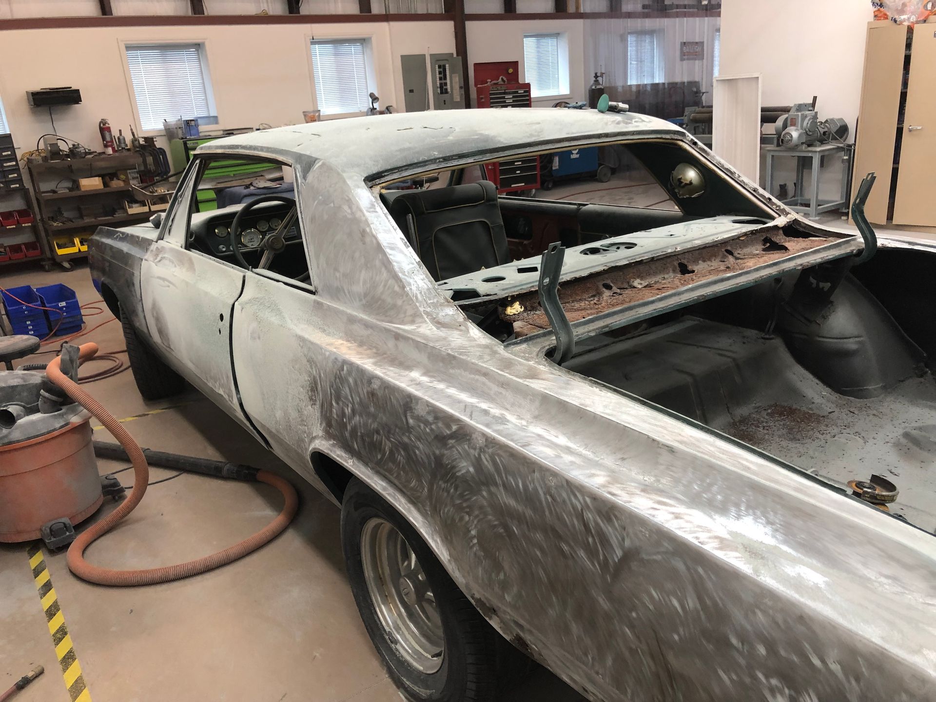 A stripped-down vintage car chassis undergoing bodywork in an auto repair shop.